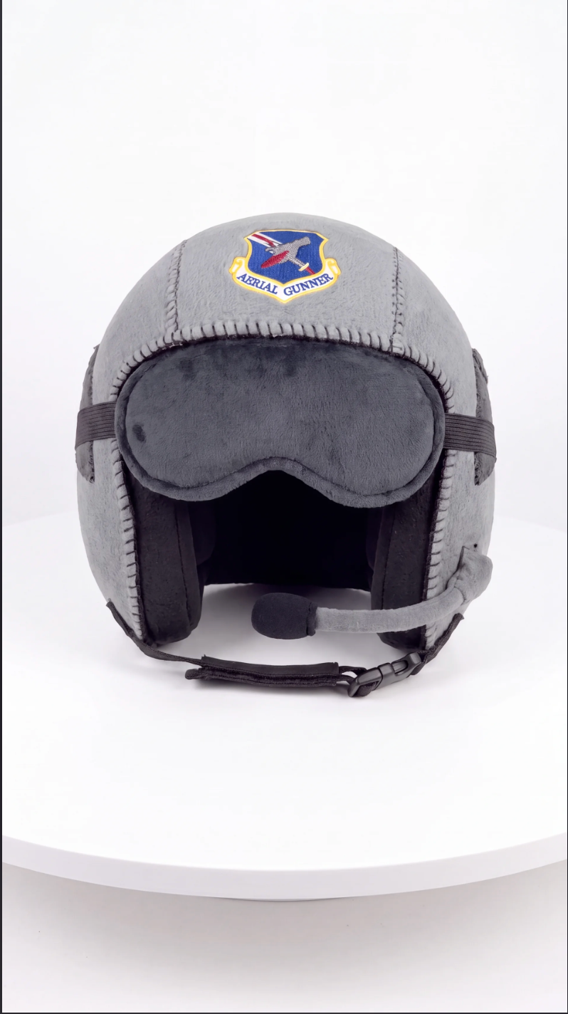 A gray military-style helmet with a dark gray face shield, black chin strap, and a visible Air Force logo patch on the forehead, displayed on a white circular platform against a white background.