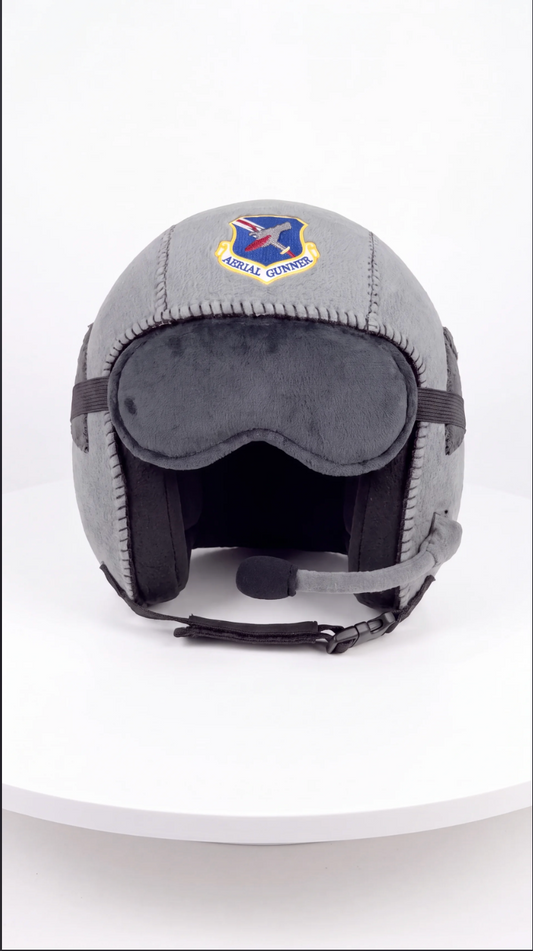 A gray military-style helmet with a dark gray face shield, black chin strap, and a visible Air Force logo patch on the forehead, displayed on a white circular platform against a white background.